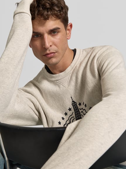 Männermodel trägt Sweatshirt mit Label-Prägung von KENZO in Beige, Rundhalsausschnitt, lockere Passform, Nahaufnahme Oberkörper.