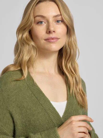 Vrouwenmodel draagt Strickjacke mit V-Ausschnitt Modell 'Petrinelle Hope' van MSCH Copenhagen in olijfgroen, relaxed fit, detailopname bovenlichaam.