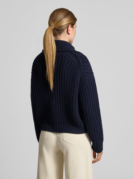 Frauenmodel trägt Strickjacke aus Wolle mit Umlegekragen von Closed in Dunkelblau, grober Strick, Zweiwege-Reißverschluss, Straight Fit, Rückansicht, Ganzkörperansicht.