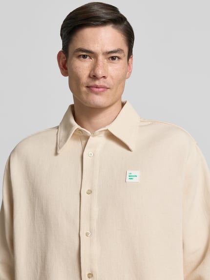 Männermodel trägt Regular Fit Freizeithemd mit Label-Patch von American Vintage in Beige, Reine Baumwolle, Kentkragen, Knopfleiste, Nahaufnahme Oberkörper. Rückenlänge 77 cm, Schulterbreite 50 cm, Ärmellänge 66 cm, Größe M/L.