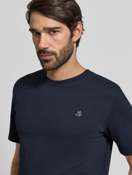 Männermodel trägt T-Shirt mit Label-Print von MARC O'POLO aus Baumwolle in Dunkelblau, gerader Schnitt, Nahaufnahme Oberkörper.