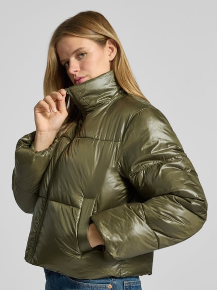 Frauenmodel trägt Puffer Jacket mit glänzender Optik von PIECES in Olivgrün, unifarben, cropped, mit Teilungsnähten und Reißverschluss, Nahaufnahme Oberkörper.