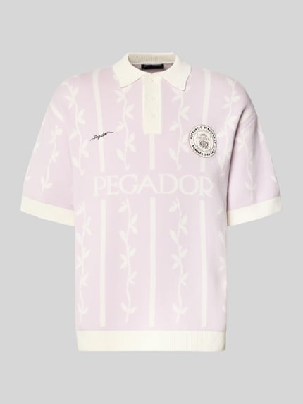 Produktfoto, koszulka polo z bawełny w odcieniach bieli i jasnego fioletu, krój relaxed fit, model 'Kinsale' od Pegador z prążkowanym kołnierzykiem polo, krótką listwą guzikową, wyhaftowanym logo i kontrastowymi krawędziami, długość tyłu w rozmiarze M: 69 cm