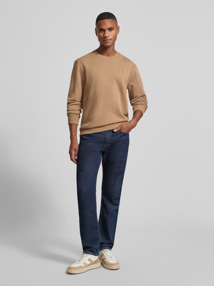 Männermodel trägt Sweatshirt mit Label-Detail von Scotch & Soda in Beige aus reiner Baumwolle, lockerer Schnitt, gerippte Abschlüsse, Rundhalsausschnitt, Rückenlänge bei Größe M 70 cm, Ärmellänge 68 cm, Ganzkörperansicht von vorne.