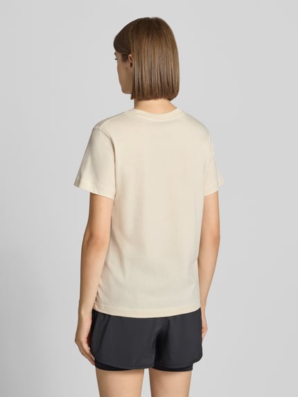 Frauenmodel trägt Regular Fit T-Shirt aus reiner Baumwolle von New Balance in Beige mit Rundhalsausschnitt, Rückenansicht, Ganzkörperansicht Rückansicht.
