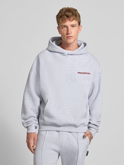 Männermodel trägt Relaxed Fit Hoodie aus Baumwoll-Mix mit Label-Detail von PROHIBITED in Hellgrau, Känguru-Tasche, Nahaufnahme Oberkörper.