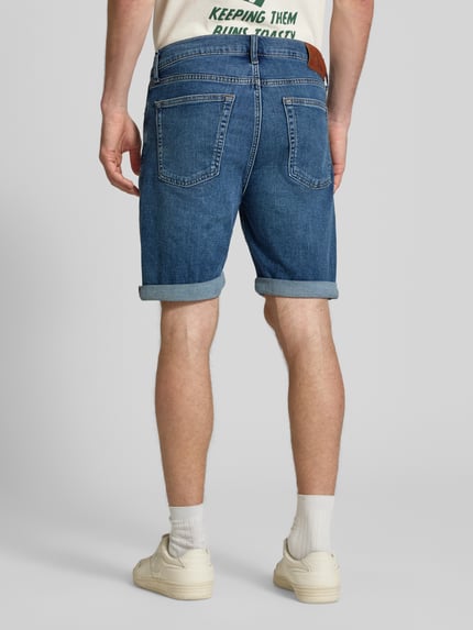Mannenmodel draagt Slim Fit Jeansshorts aus Baumwoll-Mix Modell 'HAMPTON' van Calvin Klein Jeans in denimlook met label patch, 5-pocket-design, riemlussen, knoopsluiting en omgeslagen pijpen, materiaal katoenmix, geheel lichaamsaanzicht rugaanzicht.