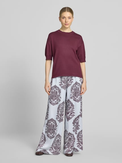 Frauenmodel trägt Wide Leg Pants mit Eingrifftaschen Modell 'Lunet' von Neo Noir, Muster in Weiß und Dunkelrot, Ganzkörperansicht von vorne. Damen Wide Leg Pants von Neo Noir, Wide Fit, elastischer Bund, französische Eingrifftaschen, Bundweite 37 cm, Innenbeinlänge 78 cm.