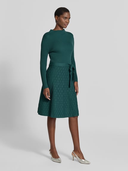 Modelka prezentuje Knielanges Strickkleid mit Bindegürtel von Apricot, Mieszanka wiskozy, linia a, długość do kolan, stójka, wiązany pasek, Długość tyłu w rozmiarze S: 103 cm, Szerokość w rozmiarze S: 38 cm, Długość rękawów w rozmiarze S: 59 cm, jednolity kolor, wzór w geometryczne tłoczenia, srebrne buty, Ganzkörperansicht von vorne