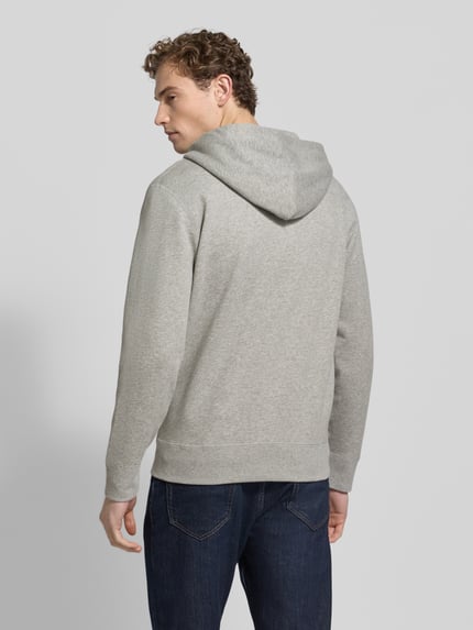 Męski model nosi bluza rozpinana z kapturem od Polo Ralph Lauren, mieszanka bawełny, luźny krój, wpuszczane kieszenie, zamek błyskawiczny, wyhaftowane logo, prążkowane wykończenia, kolor szary, faktura gładka, widok całej sylwetki z tyłu.