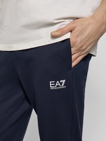 Männermodel trägt Sweatpants mit Logo und elastischem Bund von EA7 Emporio Armani in Dunkelblau, Regular Fit, Nahaufnahme Oberkörper.