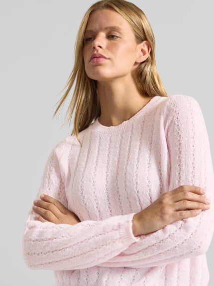 Frauenmodel trägt Regular Fit Pullover mit gerippten Ärmelbündchen Modell 'ADA' von PIECES in zartem Rosa, feine Stricktextur, Nahaufnahme Oberkörper.
