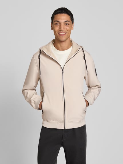 Männermodel trägt Regular Fit Jacke mit Logo-Detail von JACK & JONES in Beige, Kapuze, Reißverschlusstaschen, Ganzkörperansicht von vorne.