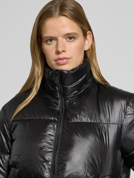 Frauenmodel trägt Puffer Jacket mit glänzender Optik von PIECES in Schwarz, sichtbar Reißverschluss, Teilungsnähte, Nahaufnahme Oberkörper.