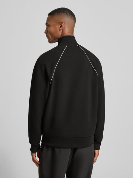 Männermodel trägt Regular Fit Sweatjacke aus Baumwoll-Mix von BOSS Green, schwarz mit Kontraststreifen, Ganzkörperansicht Rückansicht.