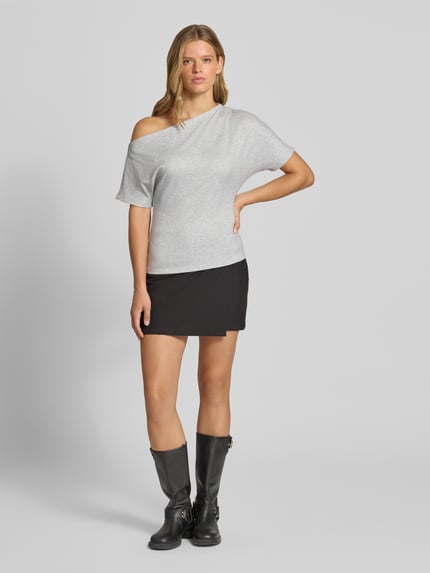 Frauenmodel trägt Regular Fit T-Shirt mit Viskose-Anteil Modell 'SILLY' von ONLY in Hellgrau, kombiniert mit kurzem schwarzen Rock und schwarzen Stiefeln, Ganzkörperansicht von vorne. Damen T-Shirt von ONLY.