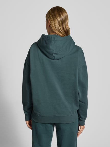 Frauenmodel trägt Oversized Fit Hoodie aus Baumwoll-Mix Modell 'CLARITA' von PEGADOR in Dunkelgrün mit Känguru-Tasche, Ganzkörperansicht Rückansicht.