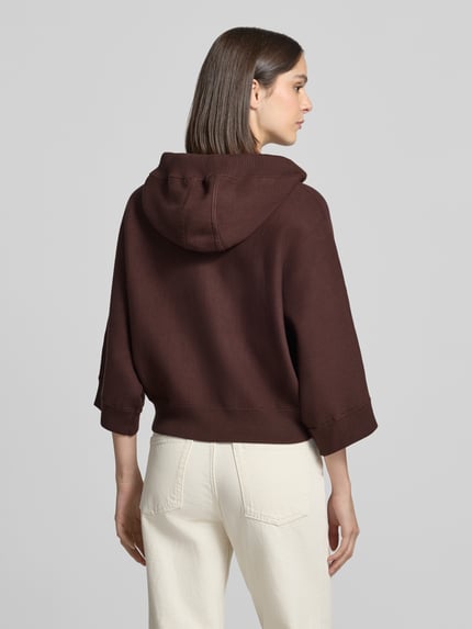Frauenmodel trägt Strickjacke mit Kapuze von Marc Cain in Unifarbe mit Animal Print und gestreiftem Innenfutter, Ganzkörperansicht Rückansicht