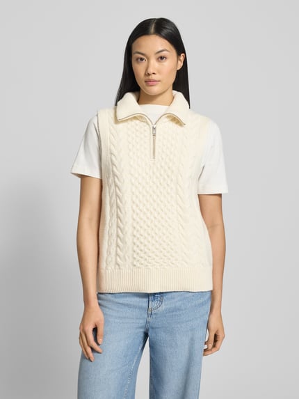 Frauenmodel trägt Relaxed Fit Pullunder aus reinem Woll-Mix Modell 'OLAIAAS CABLE' von Armedangels, Optik: Unifarben/Strukturiert, Passform: Relaxed-Fit, Troyer-Kragen, Label-Patch, Materialverarbeitung: Strick, Farbe creme, Nahaufnahme Oberkörper.