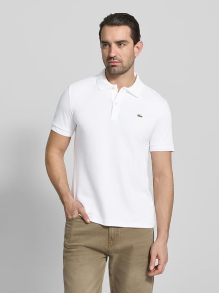 Männermodel trägt Regular Fit Poloshirt aus reiner Baumwolle von Lacoste, Optik: Unifarben, Logo-Detail, Ganzkörperansicht von vorne.