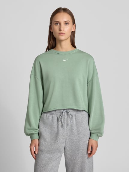 Frauenmodel trägt Relaxed Fit Pullover mit Logo-Stitching Modell 'Chill' von Nike in Mintgrün, Baumwoll-Mix, Rundhalsausschnitt, elastische Ärmelabschlüsse, graue Hose, Nahaufnahme Oberkörper.