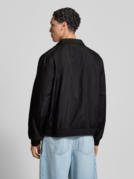 Männermodel trägt schwarze Trainingsjacke mit Logo und Stehkragen von Calvin Klein Jeans, lockerer Schnitt, glatte Struktur, Ganzkörperansicht Rückansicht.