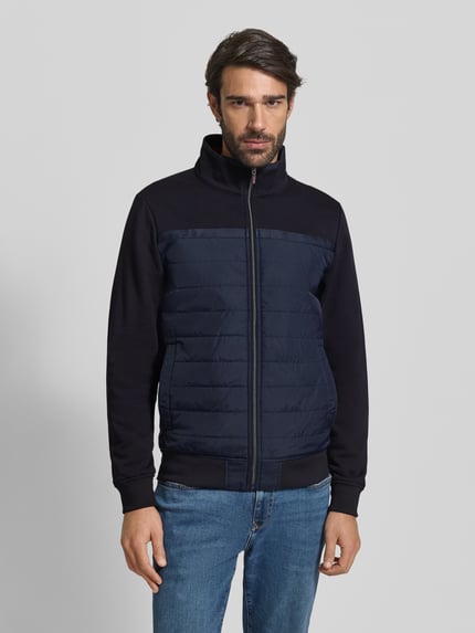Männermodel trägt Bluza rozpinana z bawełny od Christian Berg Men, krój regular fit, stójka, zamek błyskawiczny, wpuszczane kieszenie, prążkowane wykończenia, długość tyłu 69 cm, długość rękawów 67 cm, kolor granatowy, tekstura gładka i pikowana, całkowity widok z przodu.