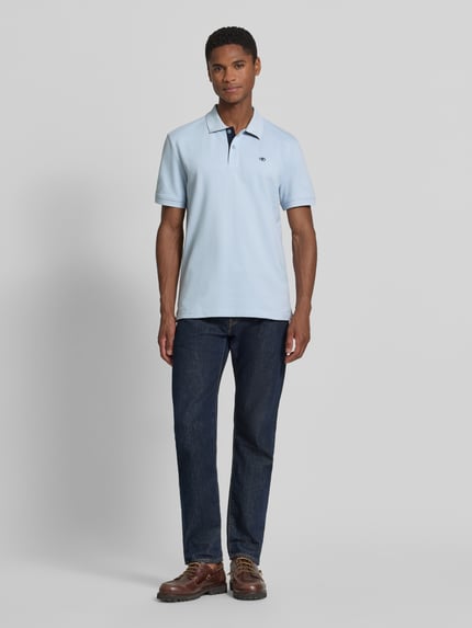 Männermodel trägt Regular Fit Poloshirt aus reiner Baumwolle von Tom Tailor in Hellblau, glatte Textur, Ganzkörperansicht von vorne.