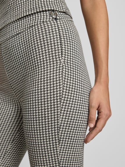 Frauenmodel trägt Slim Fit Schlaghose aus Baumwoll-Viskose-Mix Modell 'NAROSETTA' von HUGO mit Hahnentritt-Muster, Nahaufnahme Oberkörper.