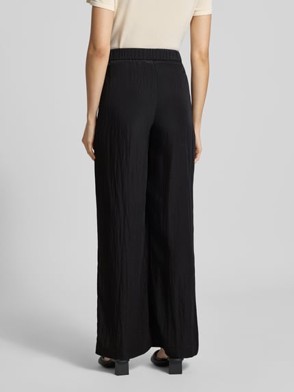 Frauenmodel trägt schwarze Stoffhose aus Viskose-Mix Modell 'Cevil' von someday mit elastischem Bund und Raffungen, lockere Passform, Ganzkörperansicht Rückansicht.
