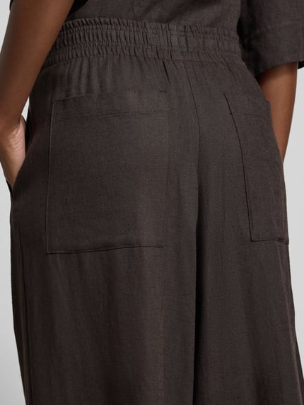Frauenmodel trägt Hose aus Leinen-Viskose-Mix Modell 'CEILING' von Drykorn in Dunkelbraun, sichtbarer elastischer Bund, Detailaufnahme Rückansicht, Damen Hose, Wide Leg, Bundweite 38 cm, Innenbeinlänge 80 cm.