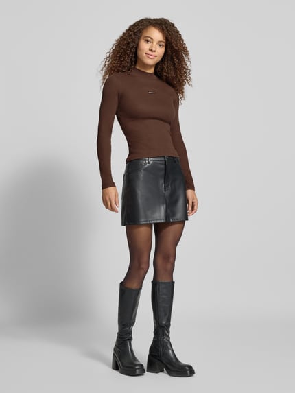 Vrouwenmodel draagt Slim Fit Langarmshirt uit katoenmix met Logopatch van GUESS, riblook, opstaande kraag, effen bruin, ruglengte maat S 53 cm, voorkant volledig zichtbaar, Ganzkörperansicht von vorne