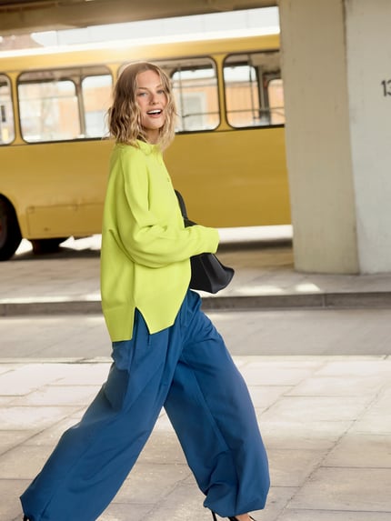 Modelka nosi Strick-Polohemd im Wide Fit - curated by Tinvcb od SIC, dzianinowa faktura, krój relaxed fit, polo kołnierz, elastyczne mankiety, długość tyłu 62 cm, długość rękawa 56 cm, jasna zieleń i niebieski, widok całej sylwetki z przodu.