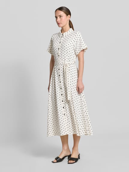 Vrouwenmodel draagt overhemdjurk met stippen, getailleerd model, overhemdkraag, knoopsluiting, strikceintuur, model 'BlakeLL' van LOLLYS LAUNDRY, midi-jurk, mouwen met omslag, ruglengte maat S 122 cm, borstwijdte 50 cm, mouwlengte 21 cm. Ganzkörperansicht van voren.