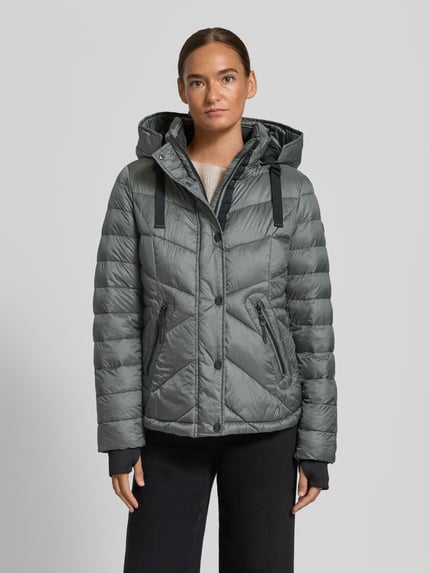 Kobiece model nosi Regular Fit Steppjacke mit abnehmbarer Kapuze od Gil Bret, szara, kurtka pikowana z lekkim połyskiem, widok całej sylwetki z przodu.