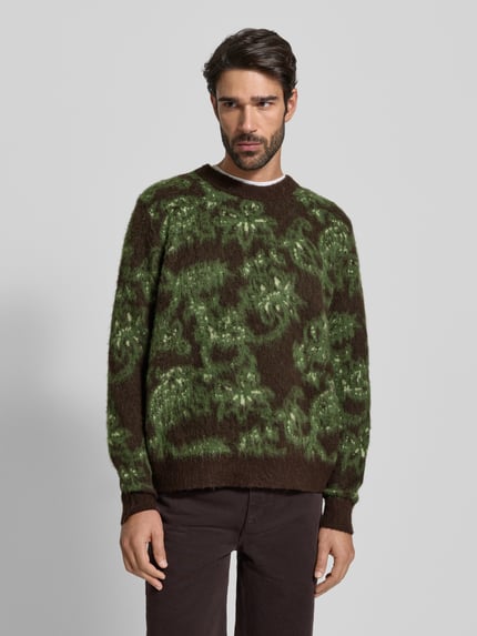 Männermodel trägt Strickpullover mit Rundhalsausschnitt Modell 'Herbert' von Wood Wood, Material-Mix mit Alpaka-Anteil, Regular-Fit, Allover-Look in Grün und Braun, weiche Textur, Rückenlänge 67 cm, Ärmellänge 67 cm, Ganzkörperansicht von vorne.
