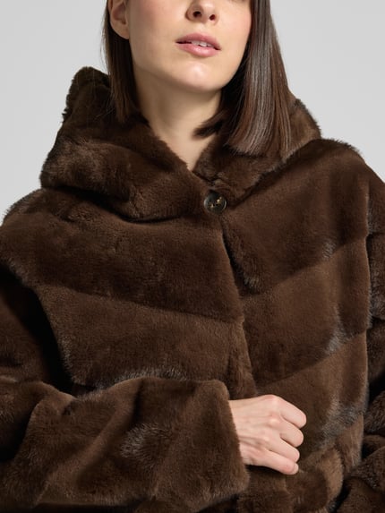 Kobiece model prezentuje Jacke mit Kapuze und Bindegürtel von Rinascimento, brązowy sztuczny futerko, krój prosty, z kapturem, zapięcie na guzik, pasek do wiązania, boczne kieszenie, długość tyłu w rozmiarze S: 70 cm, zbliżenie na górną część ciała.