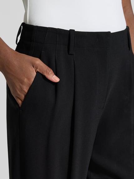 Kobieta nosi czarne spodnie materiałowe Relaxed Fit Stoffhose mit Kellerfalten od Armani Exchange, kontrafałdy, wpuszczane kieszenie, kieszeń z tyłu, zakończenia nogawek z mankietem, zapięcie na guzik i zamek błyskawiczny, Szerokość w rozmiarze 36: 42 cm, Długość wewnętrzna nogawki w rozmiarze 36: 78 cm, tekstura gładka, detaliczny widok na kieszeń przednią, Nahaufnahme biodra