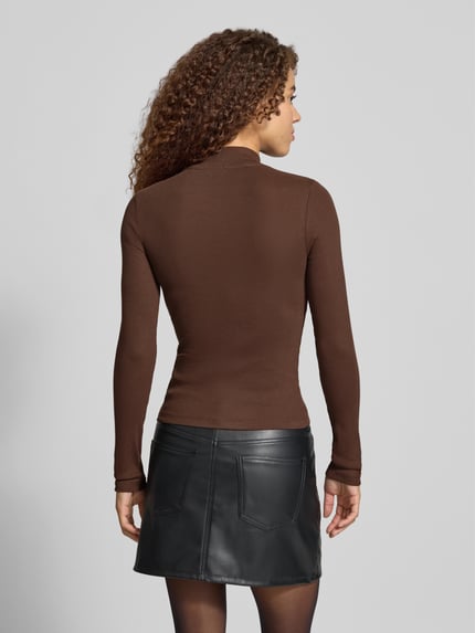 Vrouwenmodel draagt Slim Fit Langarmshirt aus Baumwoll-Mix met logo-patch van GUESS Jeans, ribstructuur, bruine kleur, rugaanzicht, context: dames langarmshirt, elastische katoenmix, slim fit, opstaande kraag, logo-label, lange mouw, ruglengte maat S 53 cm.