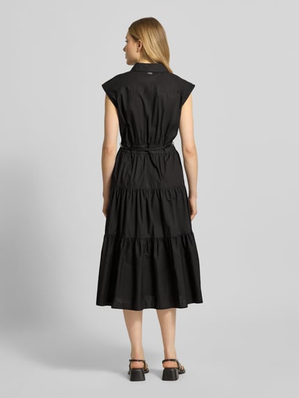 Frauenmodel trägt Hemdblusenkleid mit Gürtel und Knopfleiste von MICHAEL Michael Kors, schwarz, reine Baumwolle, Volantsaum, taillierter Schnitt, Ganzkörperansicht Rückansicht.