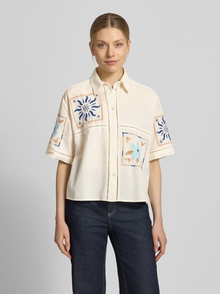 Modelka nosi Boxy Fit Bluse aus Leinen-Baumwoll-Mix von Jake*s Casual, kremowa tkanina, kolorowe hafty, kołnierz koszulowy, szeroki krój, guzik, mieszanka lnu i bawełny, długość tyłu 56 cm, długość rękawa 28 cm, widok całej sylwetki z przodu.