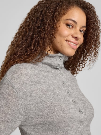 Vrouwenmodel draagt cardigan met alpaca-aandeel en opstaande kraag van Gina Tricot, materiaalmix, nauwsluitend model, knoopsluiting, ruglengte maat S 57 cm, mouwlengte maat S 72 cm, grijs gemêleerde stof, zachte textuur, detailopname bovenlichaam.