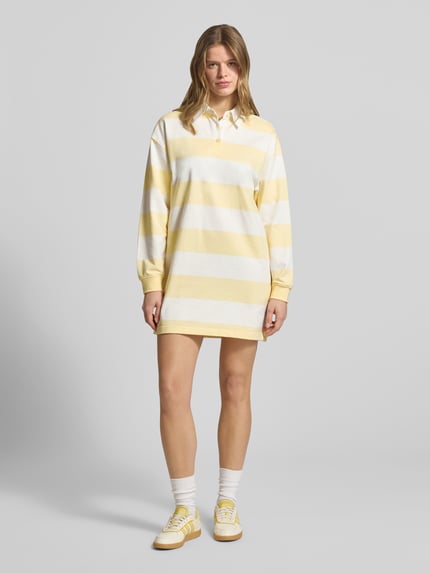 Modelka kobieca ma na sobie Sukienka mini o kroju regular fit z bawełny Calvin Klein Jeans, Model 'Varsity' z kołnierzykiem polo, długi rękaw, wyhaftowane logo, elastyczne zakończenia rękawów, żółto-białe szerokie pasy, długość tyłu w rozmiarze S: 84 cm, szerokość w rozmiarze S: 52 cm, długość rękawa w rozmiarze S: 53 cm, widok całej sylwetki z przodu.