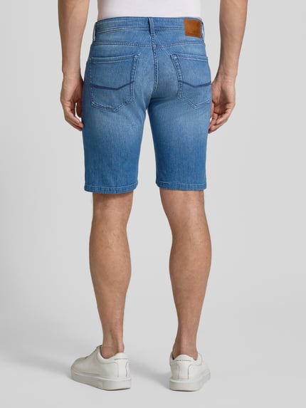Männermodel trägt Regular Fit Jeansshorts mit Eingrifftaschen Modell 'Sisteron' von Pierre Cardin, Baumwoll-Elasthan-Mix, Rückenansicht. Herren Jeansshorts, Bundweite 40 cm, Innenbeinlänge 27 cm, mittleres Blau, glatte Struktur. Ganzkörperansicht Rückansicht.
