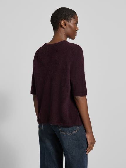 Frauenmodel trägt Relaxed Fit Strickpullover aus reiner Wolle von COMMA, dunkelviolett, weiche Textur, kurze Ärmel, Ganzkörperansicht Rückansicht. Modell 'SEPTEMBER & OKTOBER', Rückenlänge 54 cm, Ärmellänge 30 cm.