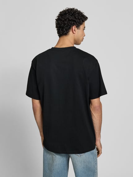 Männermodel trägt T-Shirt mit Label-Stitching und Rundhalsausschnitt von KARL KANI aus Reine Baumwolle, Oversized, Rückenlänge 77 cm, Ganzkörperansicht Rückansicht.