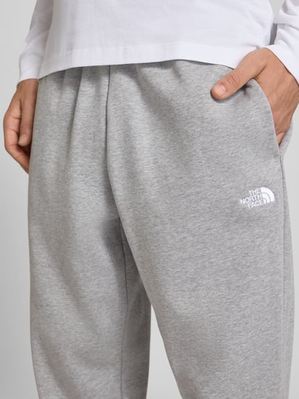 Männermodel trägt graue Relaxed Fit Sweatpants aus katoenmix Modell 'EVOLUTION' von The North Face mit steekzakken, detailaufnahme, Heren sweatpants, elastische band met tunnelkoord, binnenbeenlengte maat M 75 cm.