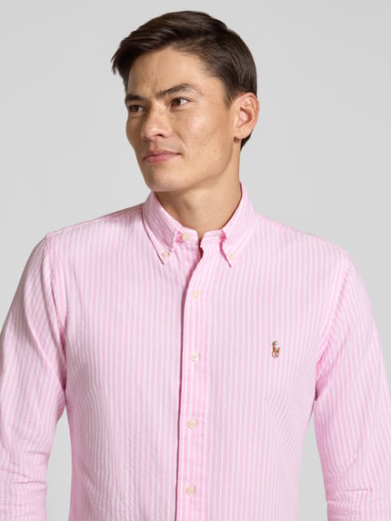 Männermodel trägt Regular Fit Freizeithemd aus reiner Baumwolle von Polo Ralph Lauren in Rosa mit weißen Streifen, Nahaufnahme Oberkörper.