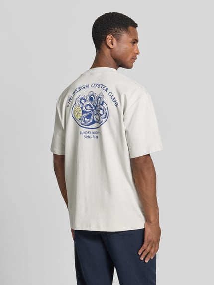 Männermodel trägt Oversized T-Shirt mit Label-Print von Lindbergh in heller Farbe aus Reine Baumwolle, Rückenlänge bei Größe M: 70 cm, Ganzkörperansicht Rückansicht.