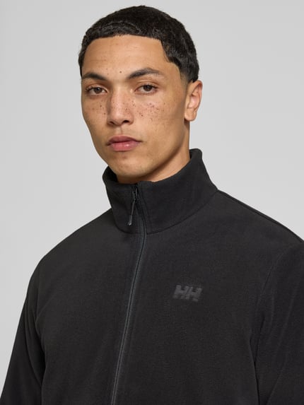 Männermodel trägt Regular Fit Fleecejacke mit Stehkragen Modell 'Daybreaker' von Helly Hansen in Schwarz, Nahaufnahme Oberkörper. Fleece, Reißverschluss, Eingrifftaschen mit Reißverschluss.